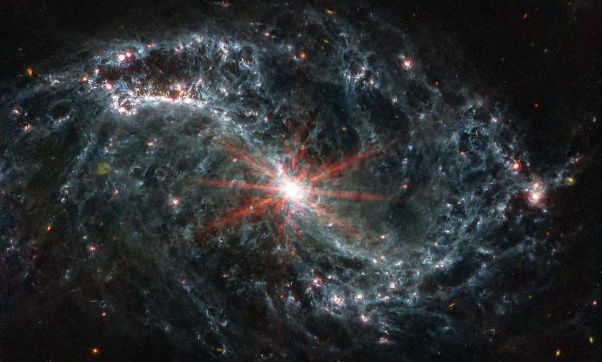 Imagen real tomada por el telescopiop espacial James Webb de una galaxia espiral gris con forma de telaraña sobre un fondo negro.