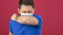 young-man-wearing-blue-polo-shirt-medical-protective-mask-sneezing-coughing-into-his-arm-elbow-prevent-spread-covid-19coronavirus-isolated-pink-wall