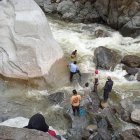La gente que acompaña a la familia de Alexis se mete en el río y busca en medio de las piedras.