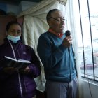 Por una ventana, el hombre, acompañado de su esposa, habla para los vecinos y recita varios versículos de la Biblia.