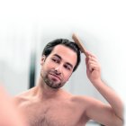 Hairstyling. Young handsome man brushing his hair and looking contented ag-dominguero