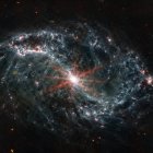 Imagen real tomada por el telescopiop espacial James Webb de una galaxia espiral gris con forma de telaraña sobre un fondo negro.