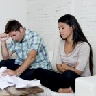 young sad couple at home living room couch calculating monthly expenses worried in stress with bank papers and documents in paying taxes , mortgage debt and cost of living concept