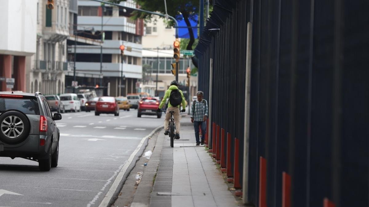 Un ciclista y un peatón comparten un espacio estrechito, a un lado de la reja.