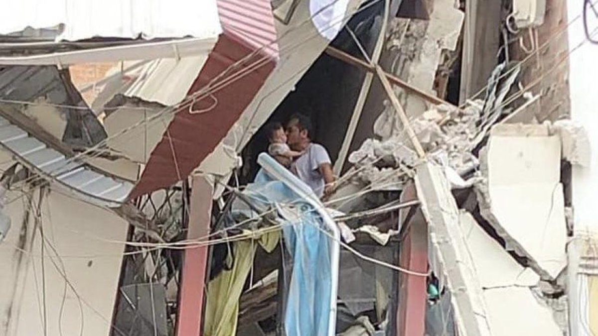 Escenario. Es un hombre, aferrádose a lo que queda de una pared y con los pies sobre una casa a punto de derrumbarse, pero quien se muestra feliz de que la vida que carga en sus brazos esté intacta.