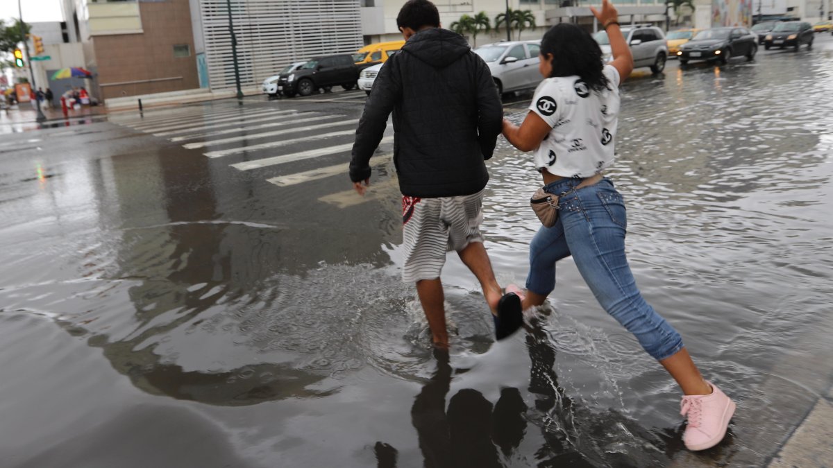 Un par de muchachos intentaban cruzar la avenida Quito sin mojarse.