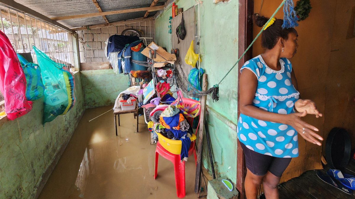 Mujer observa con preocupación la entrada de su vivienda inundada en Esmeraldas, mientras intenta proteger sus pertenencias del agua acumulada en el interior.