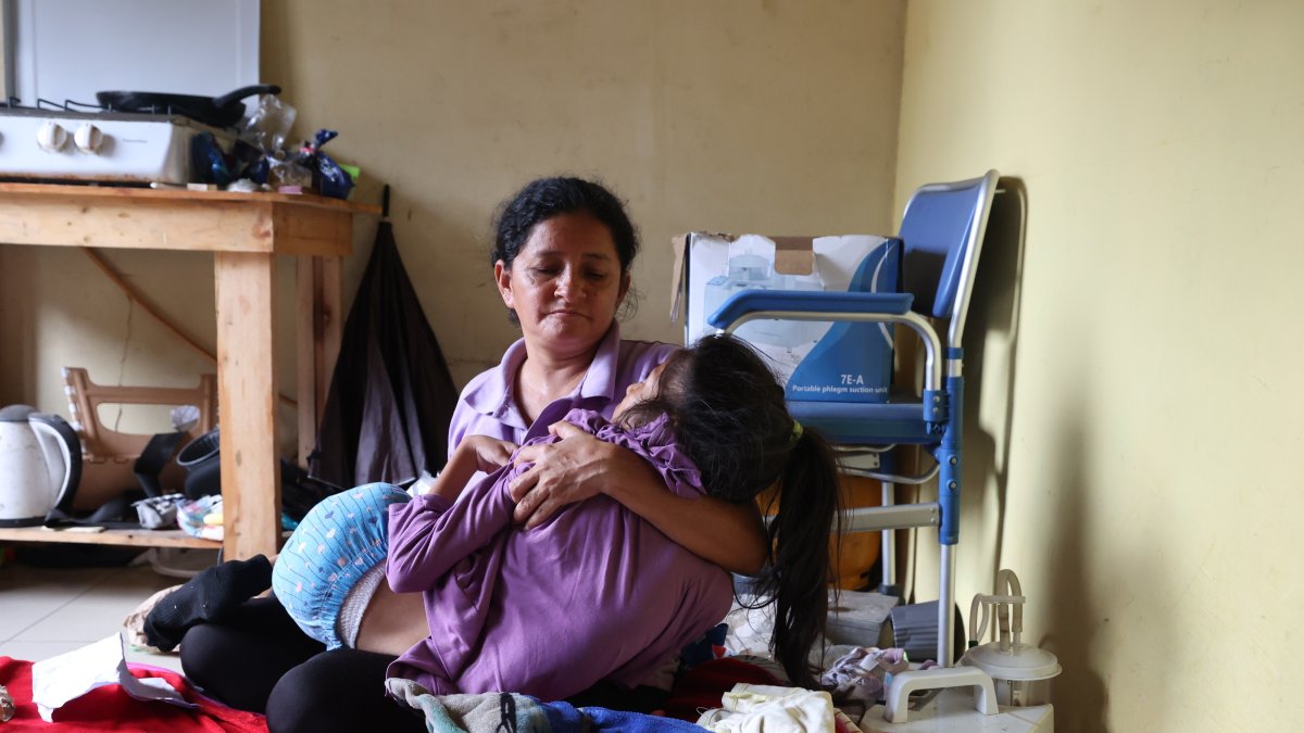 Mayra Canales sostiene a su hija, en el interior de su vivienda en Bastión Popular.