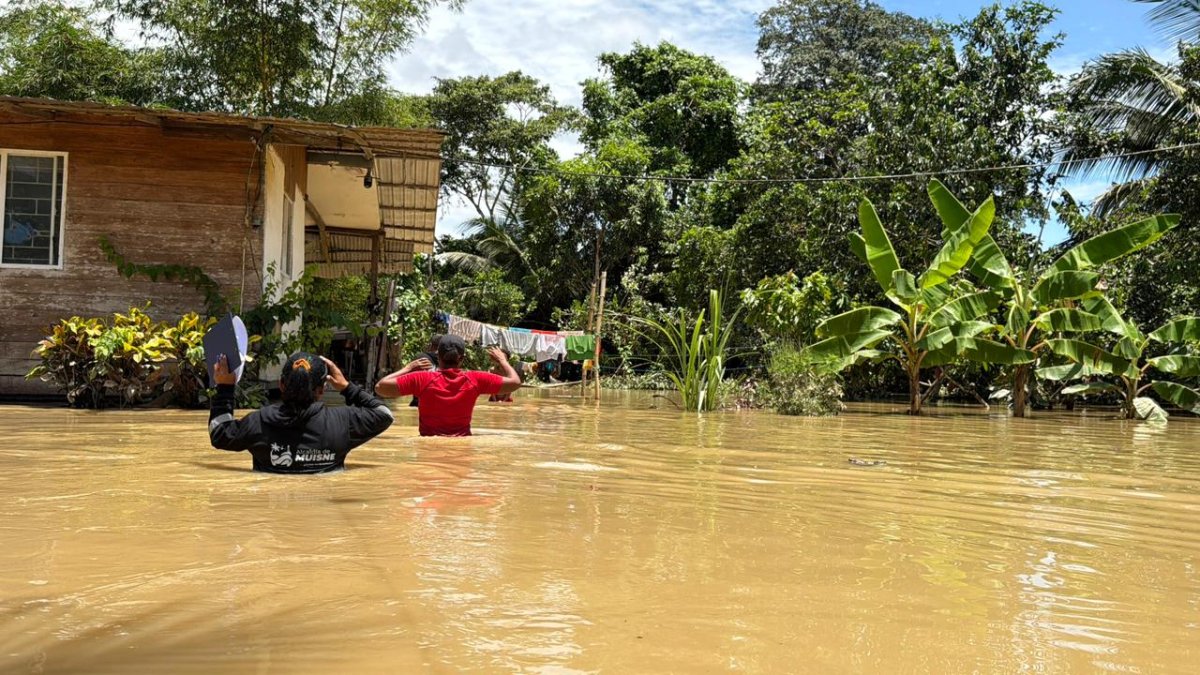 Dos personas avanzan con dificultad entre aguas turbias que cubren gran parte de la comunidad de San Gregorio, mientras viviendas y cultivos permanecen bajo el nivel de la inundación.