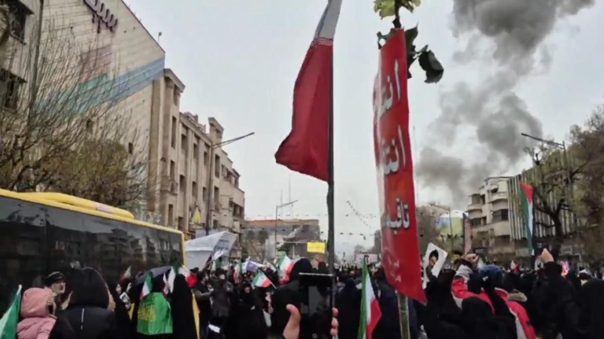 Manifestantes marchan en Teherán mientras humo de una explosión se observa a lo lejos