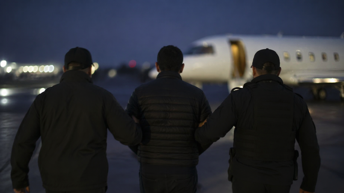 Traslado de un detenido hacia un avión bajo custodia en pista aeroportuaria nocturna, en recreación de IA.