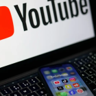 Pantalla con el logo de YouTube, propiedad de Alphabet, y un móvil con aplicaciones de redes sociales como Instagram y Facebook